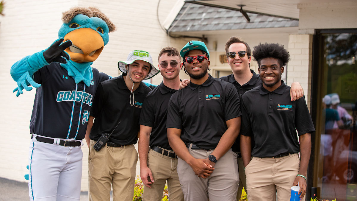 tudents stand together with a campus mascot during a university event, representing event staffing and engagement within a recreational or sports management setting.